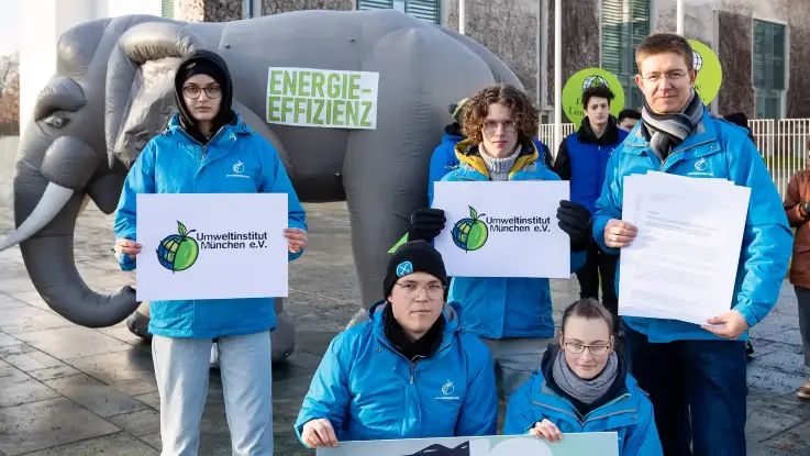 Fünf Menschen in blauen Jacken präsentieren im Freien das Logo des Umweltinstituts; hinter ihnen die Skulptur eines Elefanten, darauf steht «Energieeffizienz».